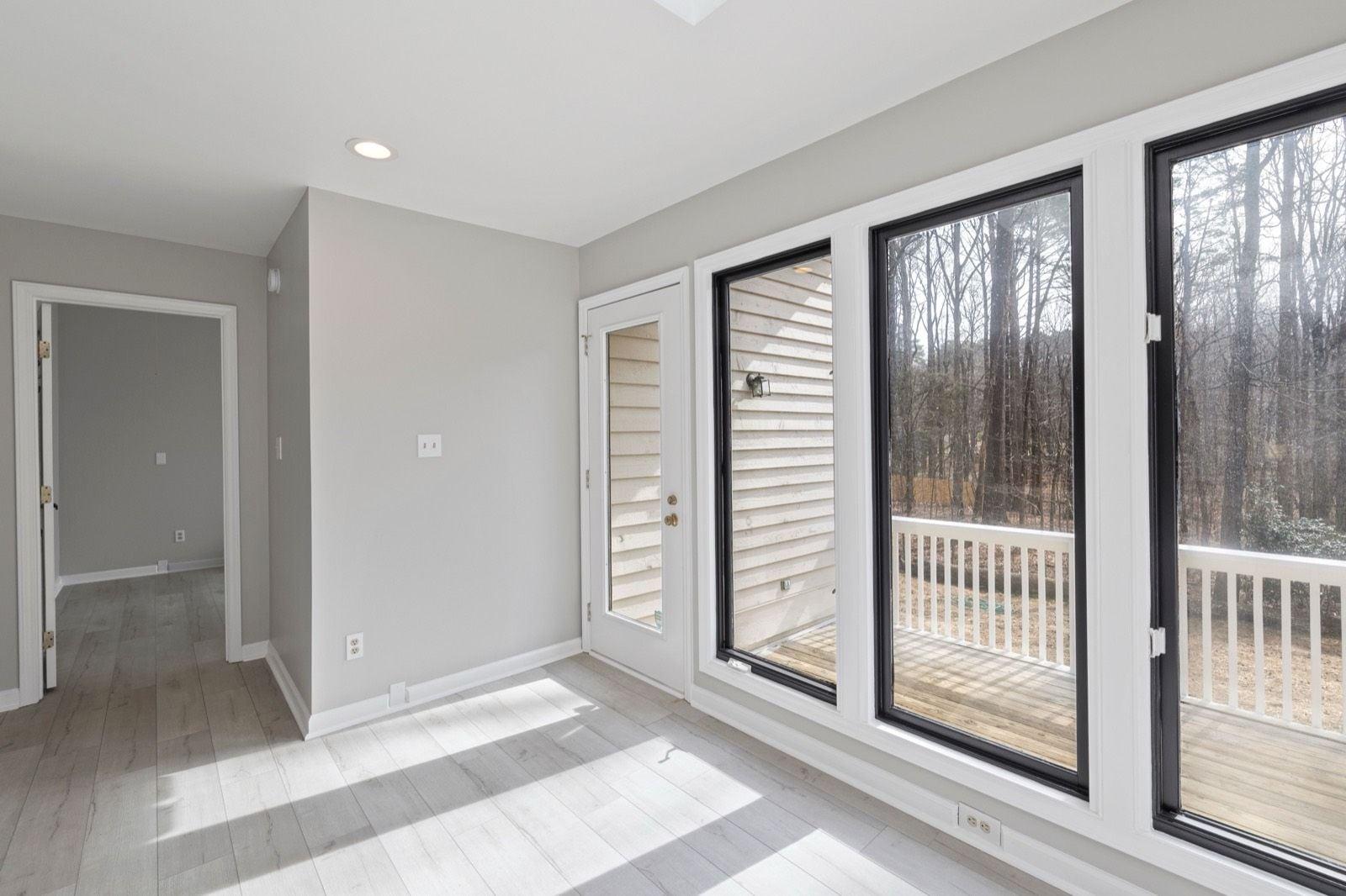 Sunlit room with smooth warm gray walls, white baseboards and trim, and large windows onto a wooden deck