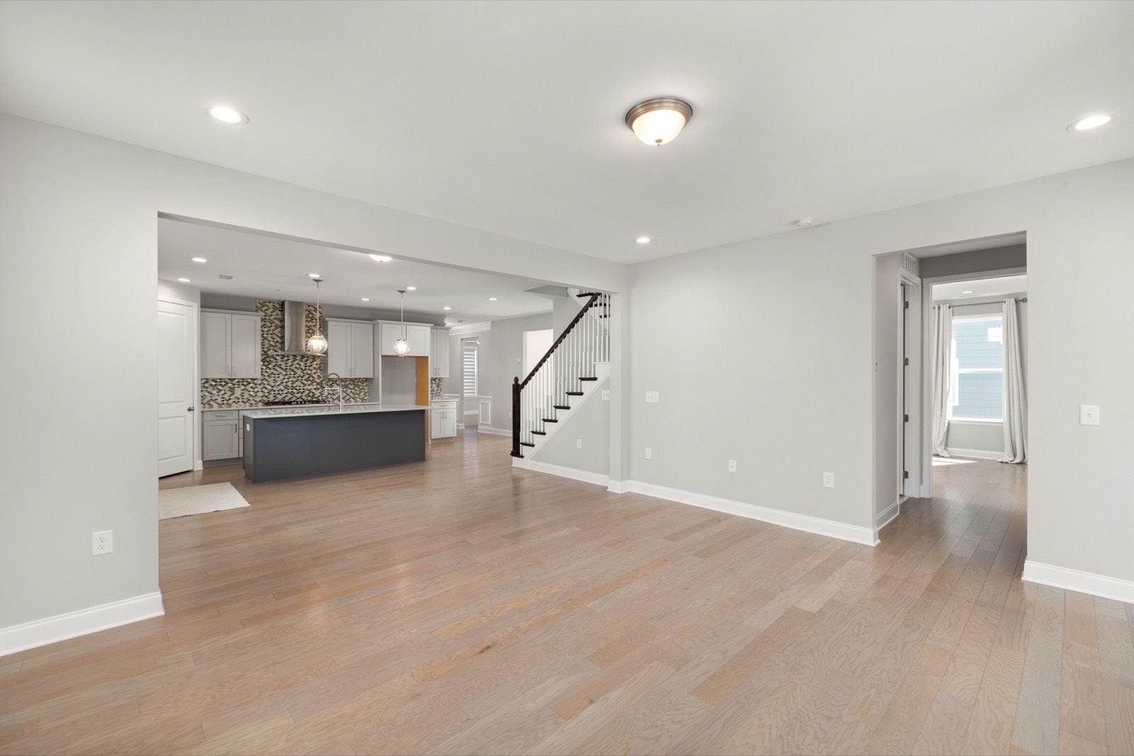 Open living area with light gray walls, white baseboards and a staircase leading to the kitchen