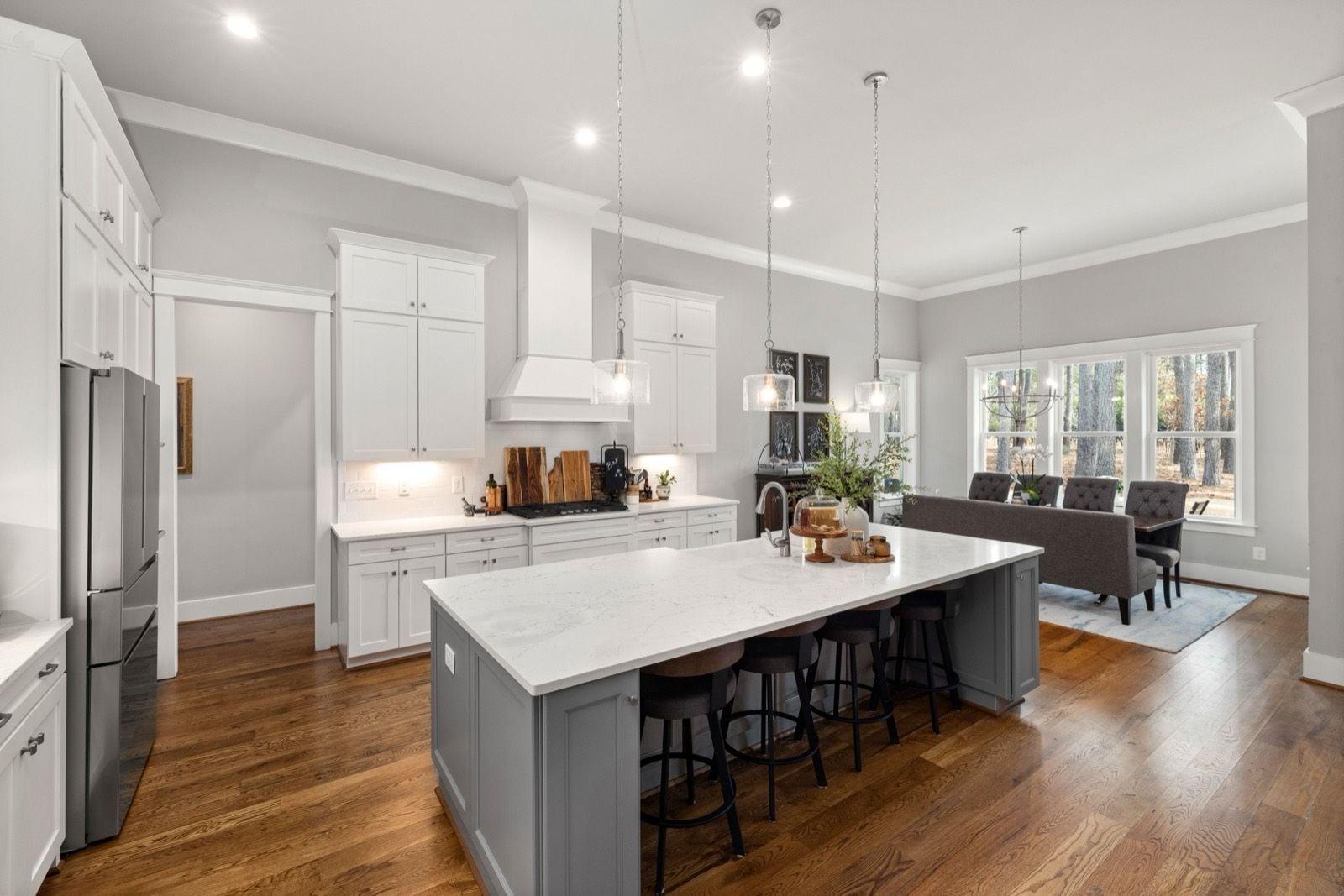 Bright open kitchen and dining area with soft gray walls, white crown molding and trim, and a gray island