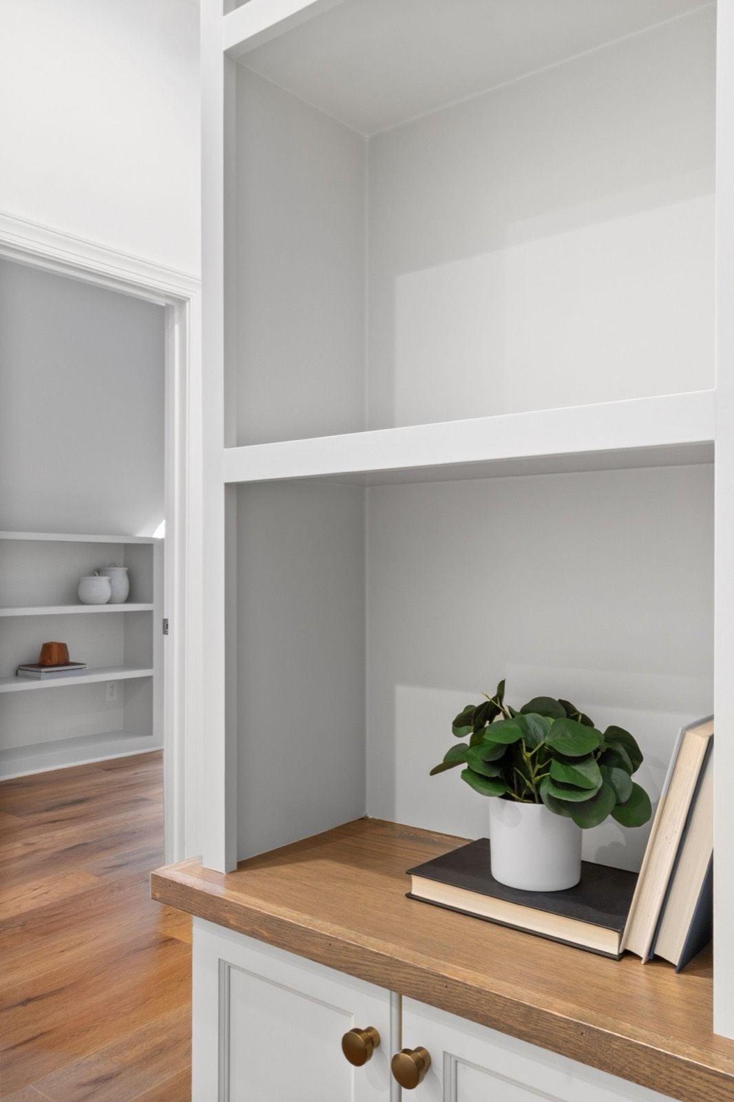 Close-up of gray painted built-in shelves and white cabinet doors with brass knobs and a wood top