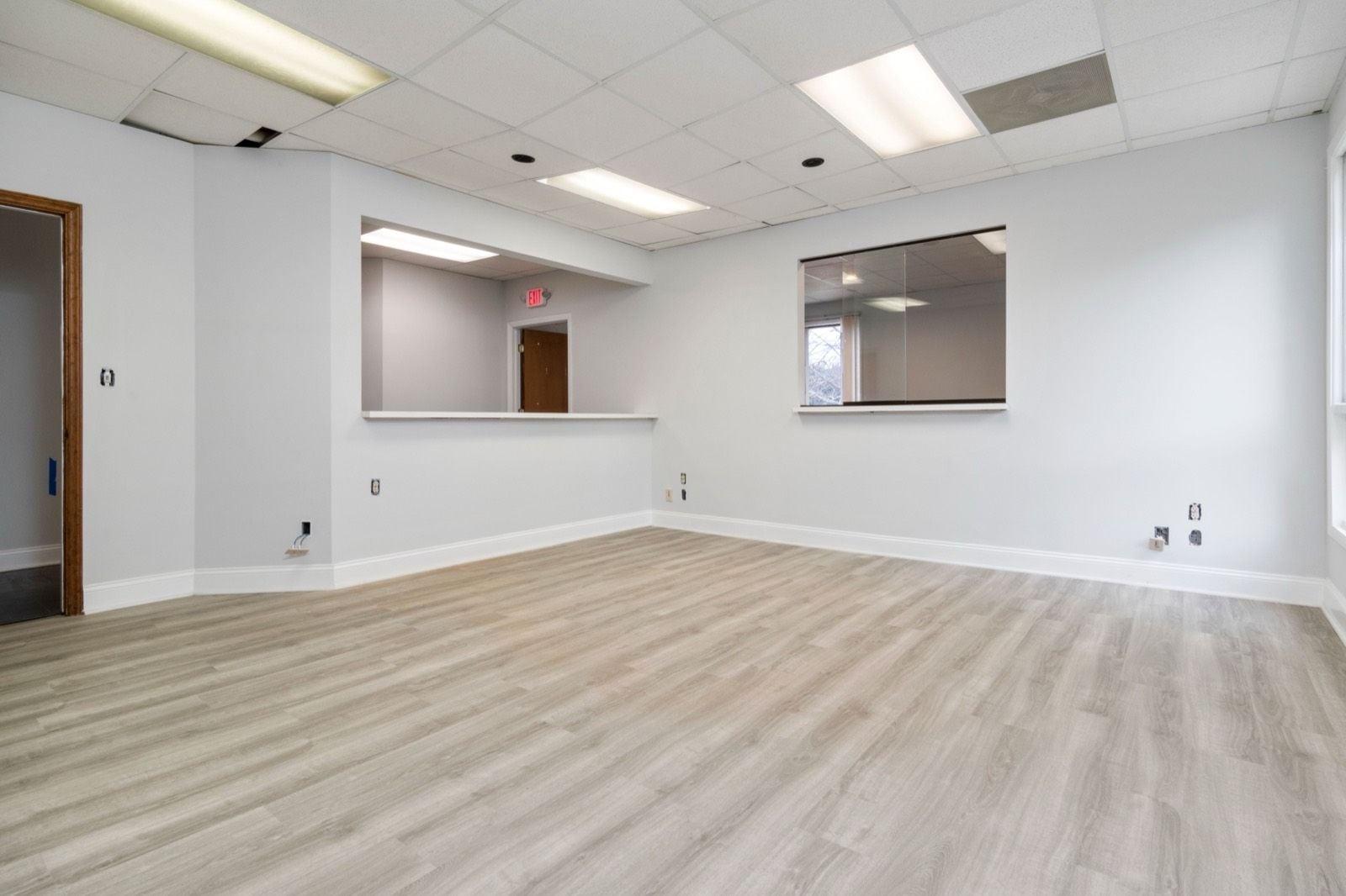 Empty commercial office suite with smooth pale gray walls, white baseboards and a drop ceiling