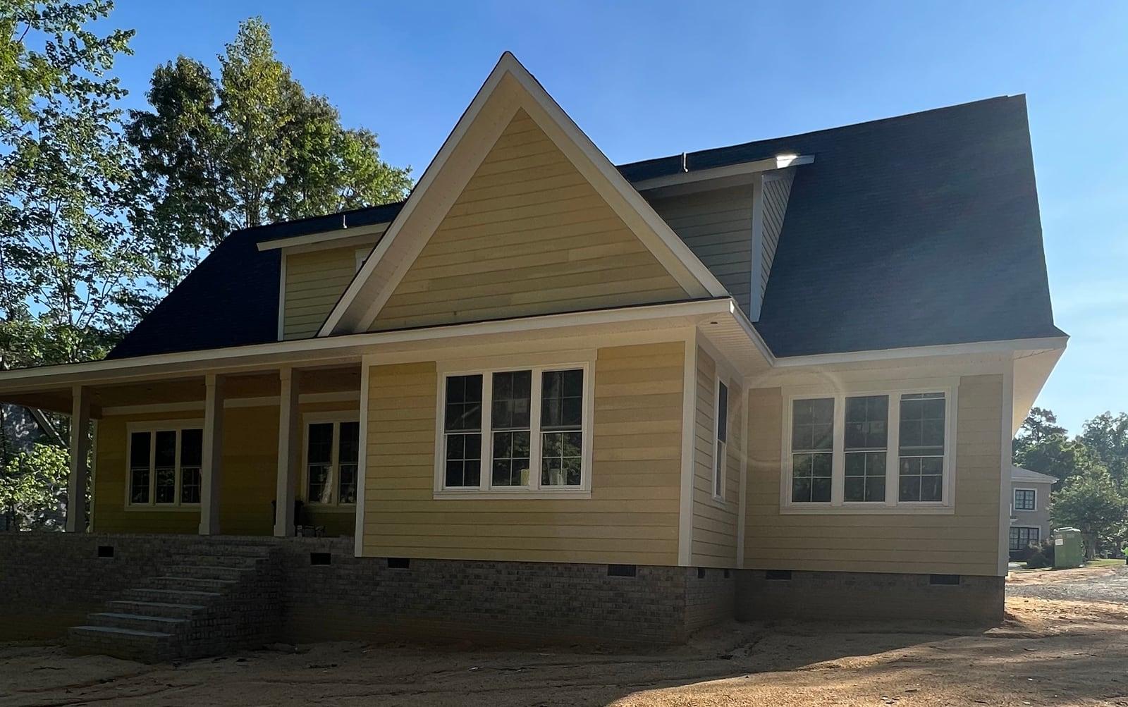 Yellow-tan lap siding with crisp white trim and window casings on a new two-story home under blue sky