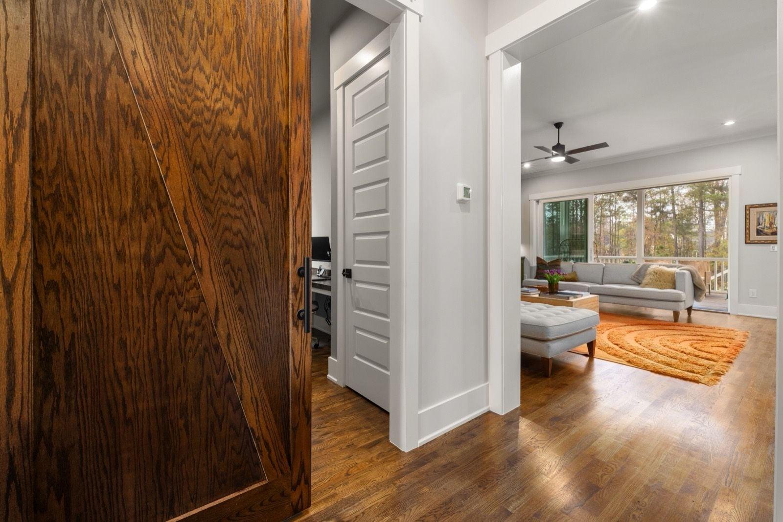 Stained wood barn door beside crisp white door casing, baseboard and a white panel door in a hallway
