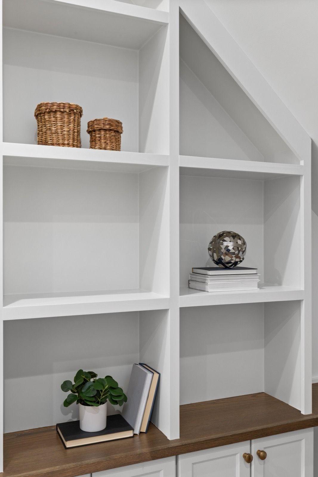 White painted built-in shelving with an angled stair cut-out above white cabinet doors