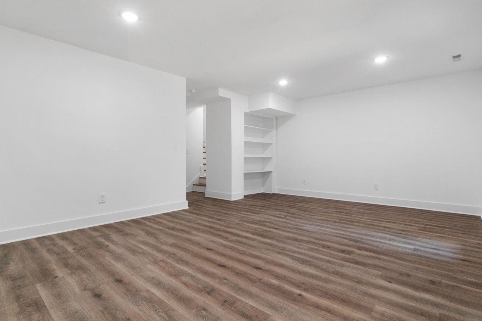 Empty basement room with freshly painted white walls, ceiling, baseboards and built-in shelving