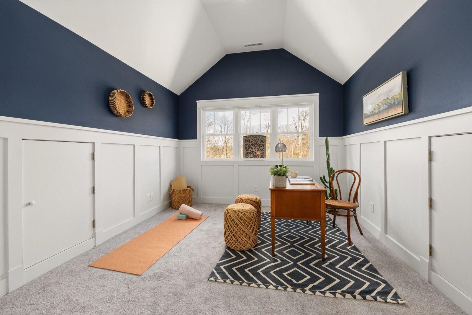 Vaulted room with navy blue walls above white board-and-batten wainscot, white cabinet doors and a wooden desk