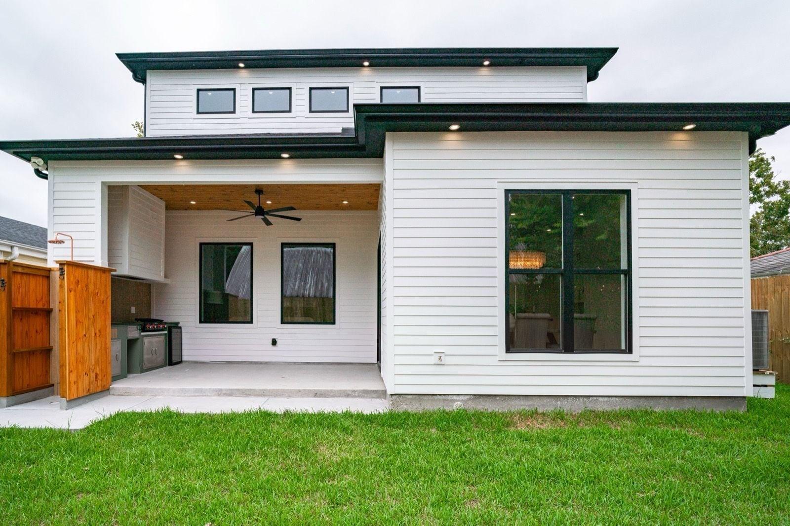 Rear of a modern home with white lap siding, black window trim, covered patio and stained wood privacy screen