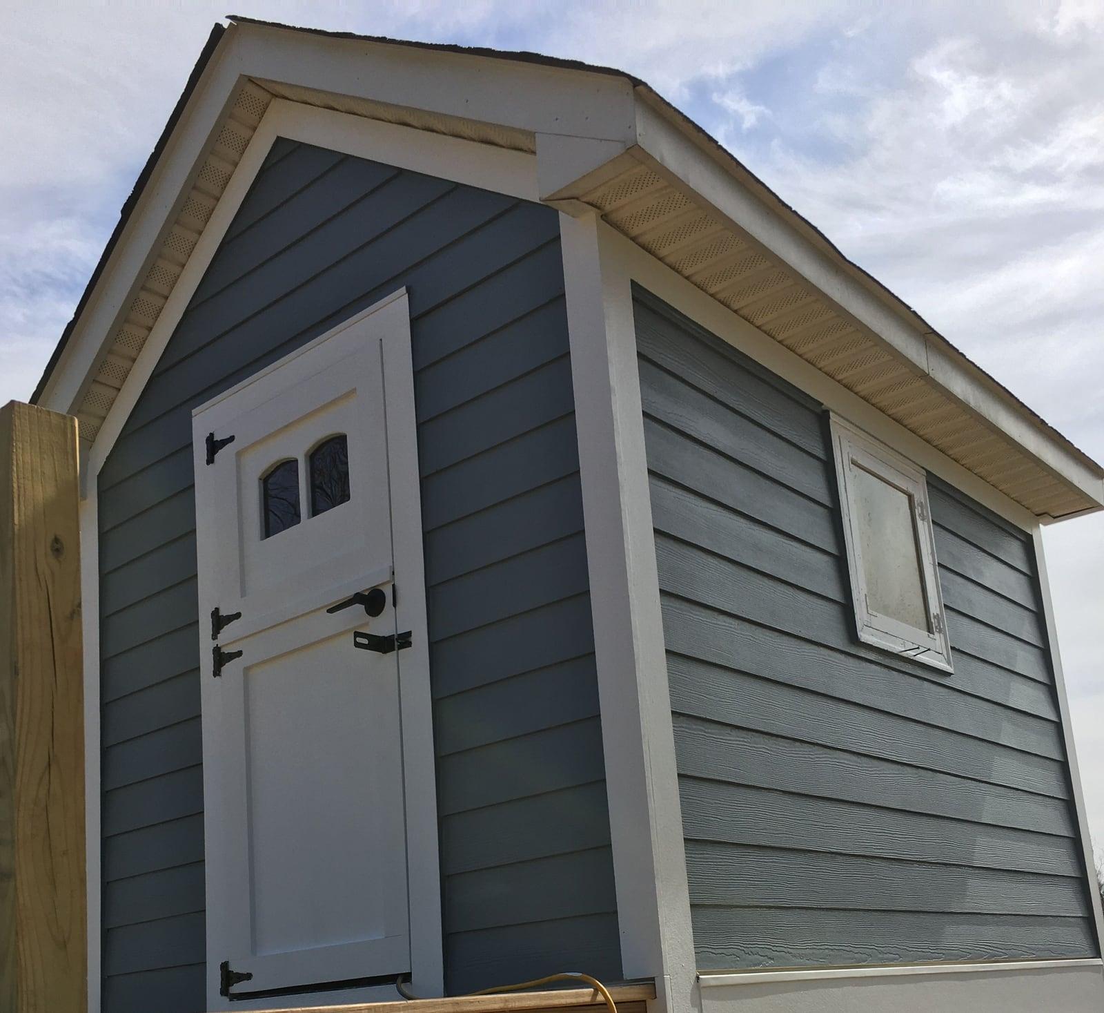 Slate-blue painted siding with white trim and a white Dutch door on a small raised cabin